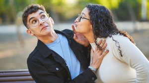 Man rejecting a woman while she tries to kiss him during a date in a park.