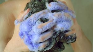 Young man washing his hair with a purple shampoo