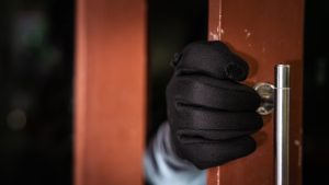 dangerous masked burglar with crowbar breaking into a victim's home door