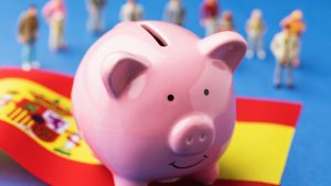 Piggy bank, flag and plastic toys on a colored background, the concept of the income of the Spanish population