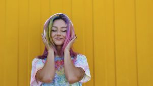 Smiling woman enjoying music listening through wireless headphones in front of yellow wall