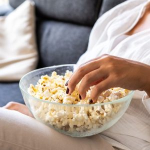 Detail of a young woman eating popcorn on the sofa in her living room.