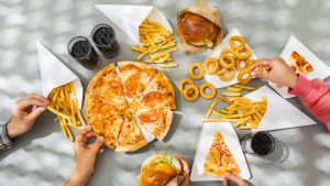 Human hands with assorted take out food such as pizza, french fries, onion rings, burger and cola.
