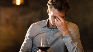 Businessman having a headache while drinking red wine in a bar.