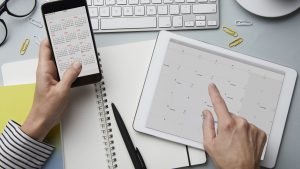 Top view of woman holding smartphone and tablet with calendar on desk