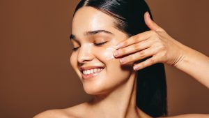 Happy with her skincare routine: Woman in her 20’s applies beauty cream on her face