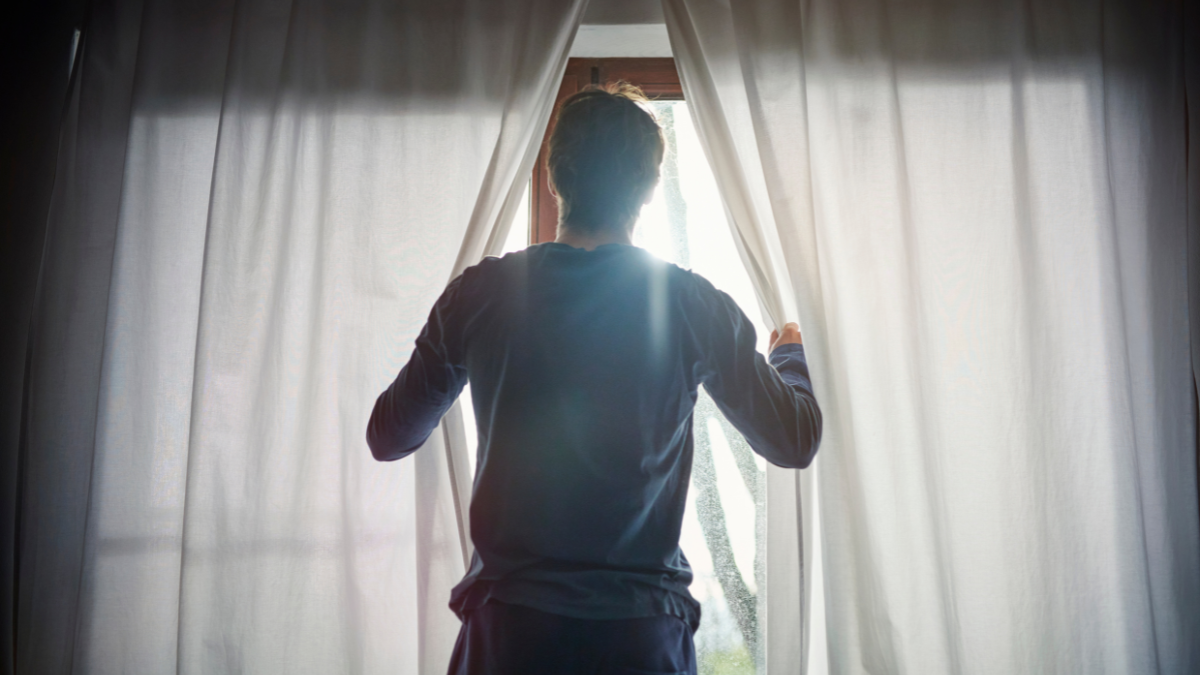Hombre abriendo las cortinas en su casa. (Getty: Uwe Krejci)