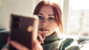 Woman with red hair looking on screen of her mobile phone.