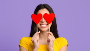 Love. Romantic asian woman posing with red hearts over eyes and smiling