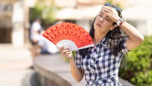 Woman uses hand fan to cool down when summer heat wave hits the city.