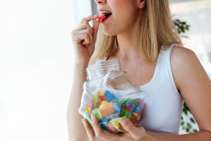 Pretty young woman eating colorful jelly candies at home. Addiction concept.