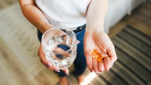 The girl holds vitamins and a glass of water in her hand. Morning rituals. Water. Glass of water. Water balance in the body. Vitamins. Vitamins and dietary supplements.