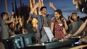 Portrait of young couple dancing with disc jockey playing in foreground