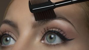 Young woman brushing eyebrows, close up.