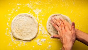 Man's Hands Kneading a Homemade Pizza Dough on a Yellow Background full of Flour