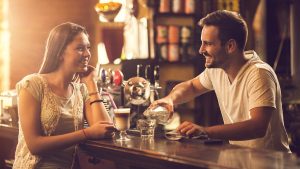 Happy bartender pouring a drink while flirting with female customer.