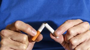 Hands Breaking Cigarette On Blue Background. New Year Resolution.