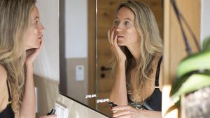 Woman applying makeup in front of bathroom mirror