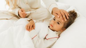 Mother checking temperature of her sick dauther with hand and thermometer.