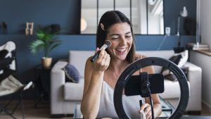 Happy influencer recording make-up tutorial on smart phone at home