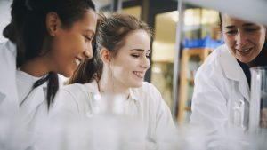 Happy mature teacher with young multi-ethnic female students learning at chemistry laboratory
