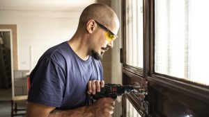 Locksmith changes a lock at home with a battery drill