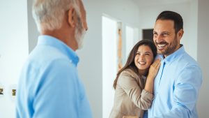 Friendly Real Estate Agent and young couple shaking hands standing in hallway