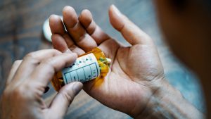 Close-up of a male hand holding a pill bottle pouring medication into his hand