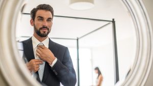 Mirror reflection of young businessman adjusting shirt and tie in hotel room, Dubai, United Arab Emirates