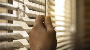 Person at home lowering the blinds to keep out the sunlight due to a summer heat wave in the city. Slat blinds to protect from the sun and keep the room cool due to the heat wave. Heat wave concept