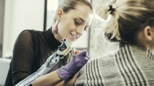 female tattooist tattooing upper arm of female customer