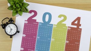 Top views of the Desk Calendar 2024:  Calendar is used to plan daily work and life with houseplant and alarm clock against a wooden table background.