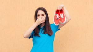 Woman Covering Nose Holding a Pair of Stinky Shoes
