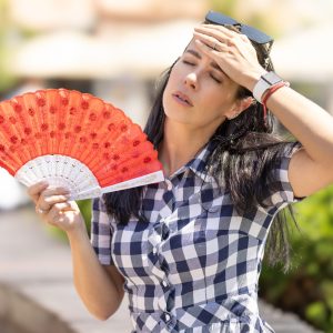 Woman uses hand fan to cool down when summer heat wave hits the city.