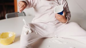 toddler over a table eating a yogurt and messing up