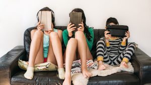 three kids with electronic devices on a sofa