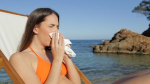 Sick tourist blowing nose with tissue on beach
