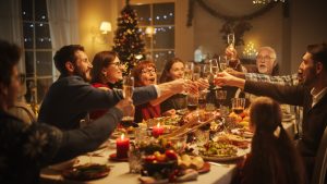 Portrait of a Handsome Young Black Man Proposing a Toast at a Christmas Dinner Table. Family and Friends Sharing Meals, Raising Glasses with Champagne, Toasting, Celebrating a Winter Holiday